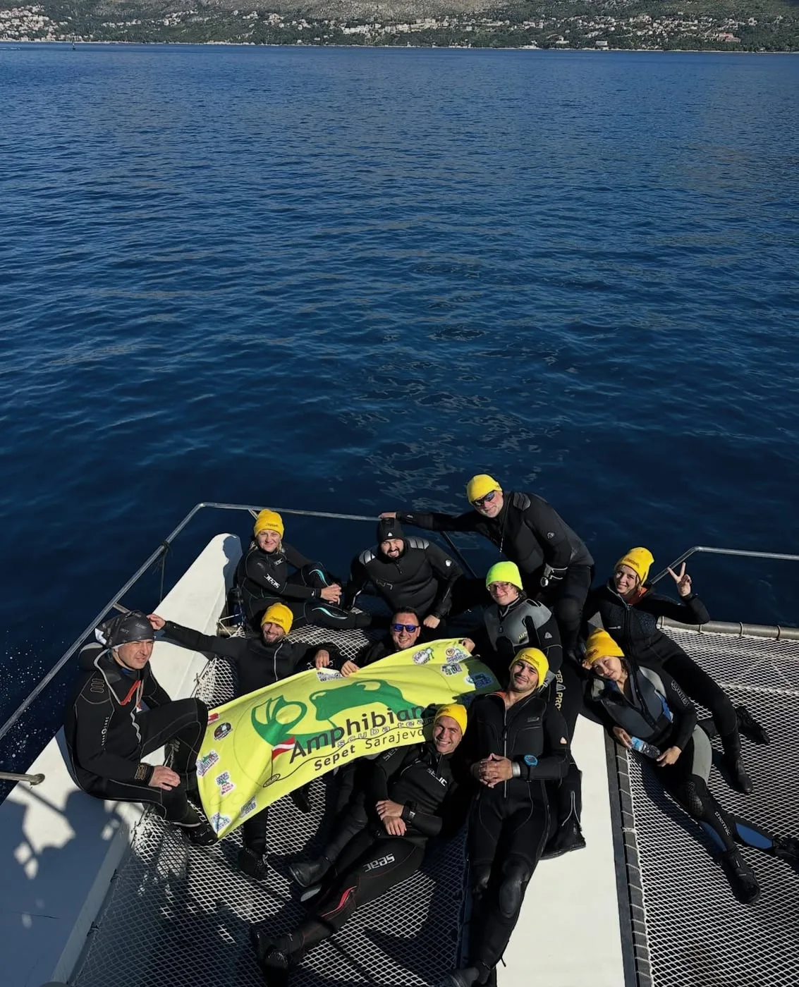 Scuba diving team in wetsuits on a boat deck, holding a club flag