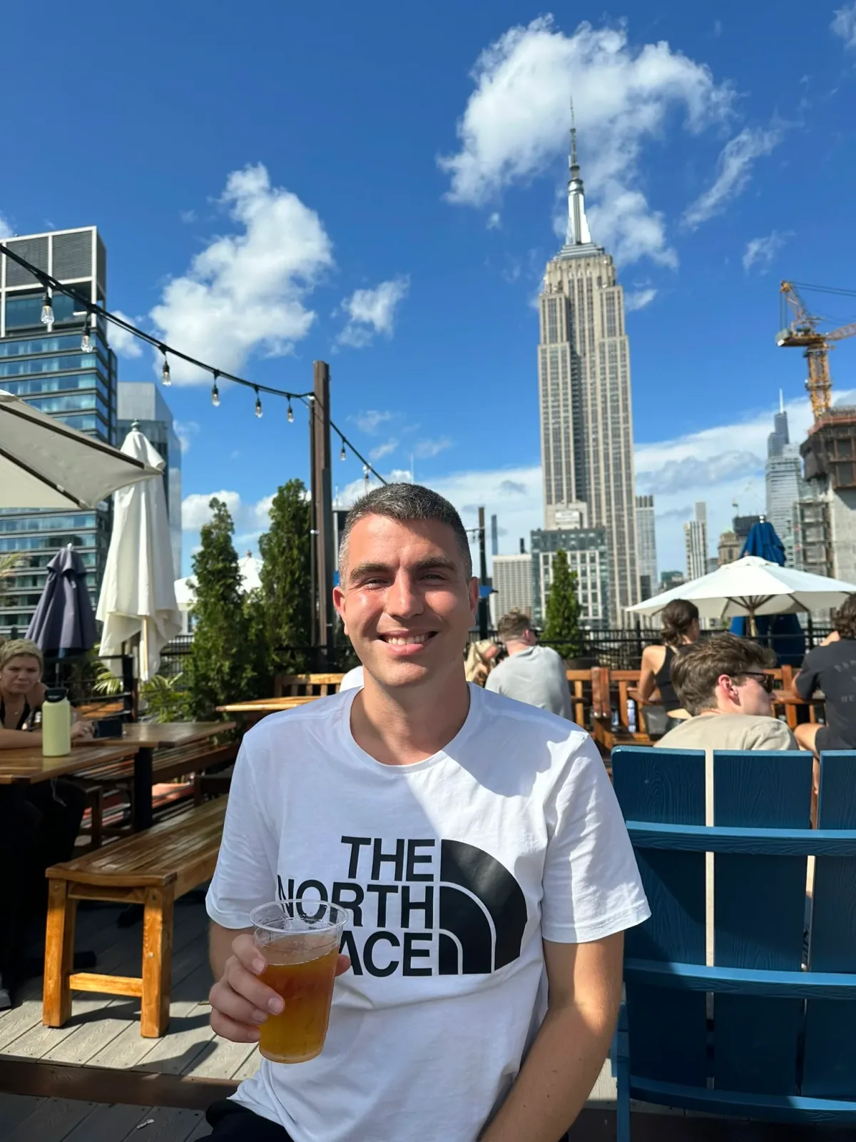Dejan with a beer on a New York rooftop, the Empire State Building behind him